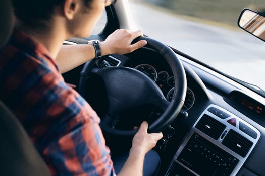 Chico conduciendo a los mando de su vehículo, con una postura de conducción correcta